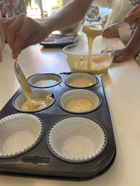 Muffinteig wird mit einem Löffel in Papierförmchen im Muffinblech gefüllt